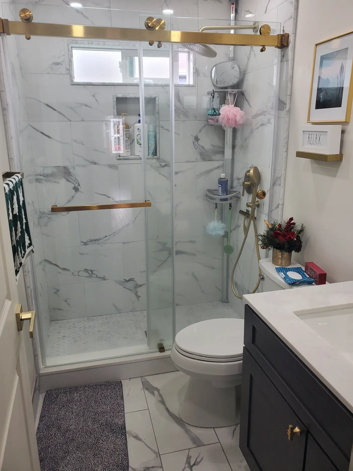 The same Rodeo bathroom after remodeling, with a full-height marble-look tiled walk-in shower, glass door, brass fixtures and a new vanity
