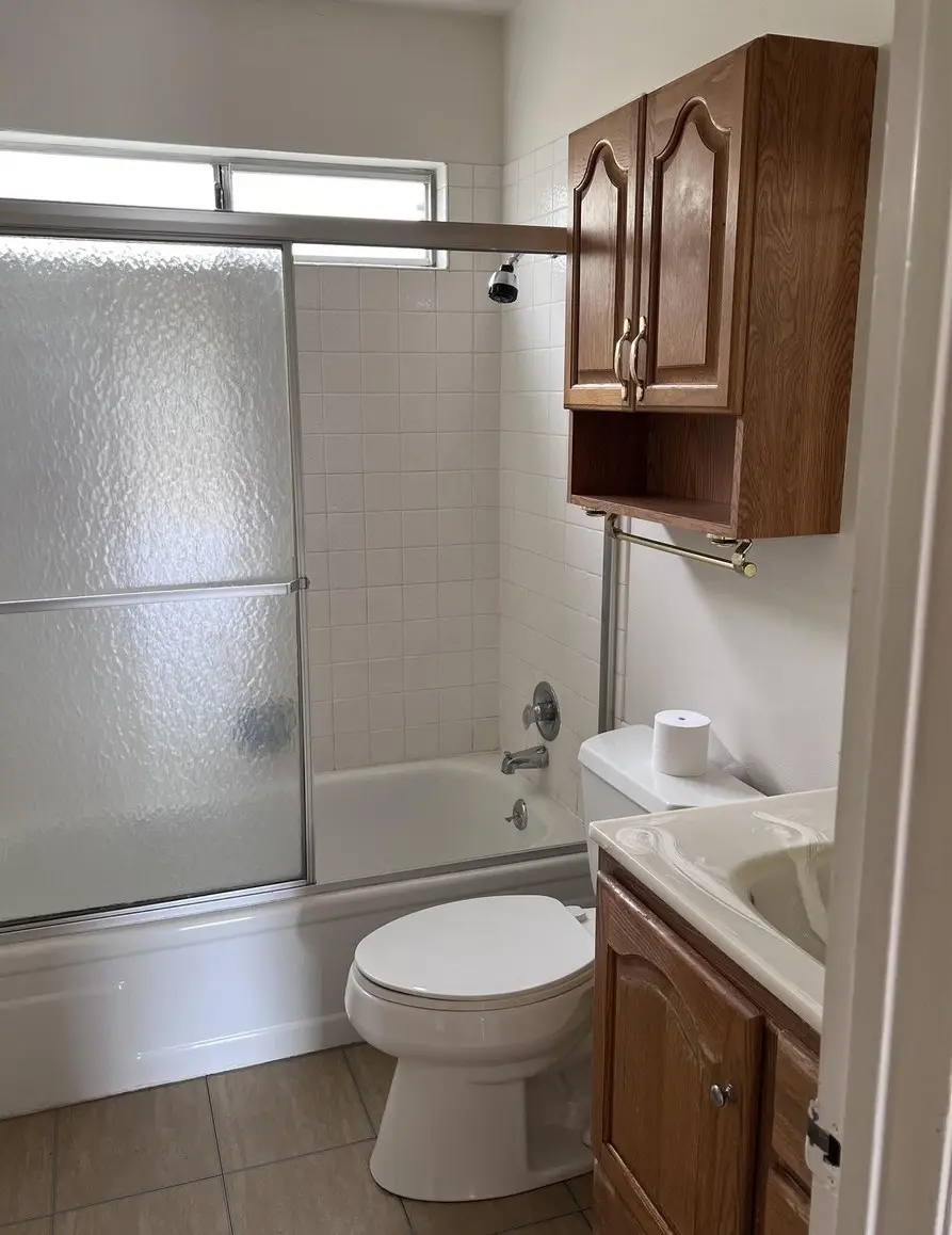 Original 1970s bathroom in Rodeo with a tub-and-tile surround, sliding glass shower door and a dark oak vanity