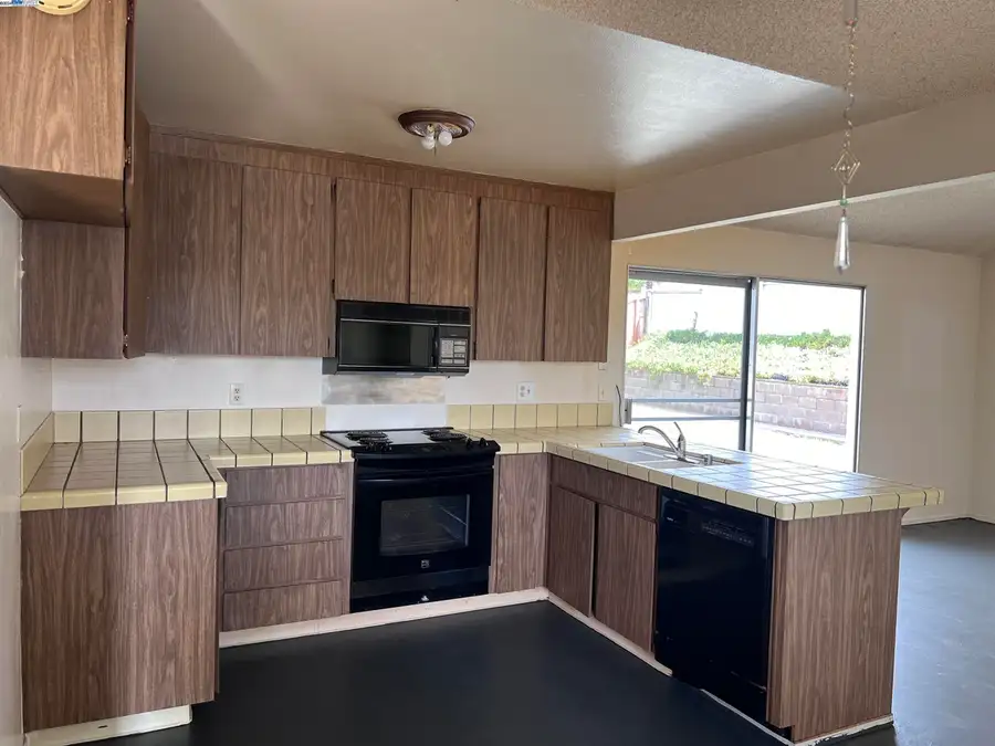 An original 1970s kitchen in Rodeo with woodgrain laminate cabinets, tile countertops and a black range, before remodeling