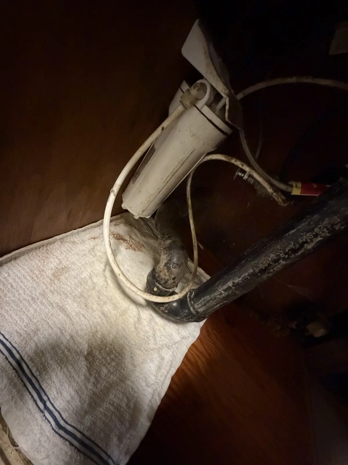 Under-sink water filter canister with staining on the cabinet base and a towel beneath it