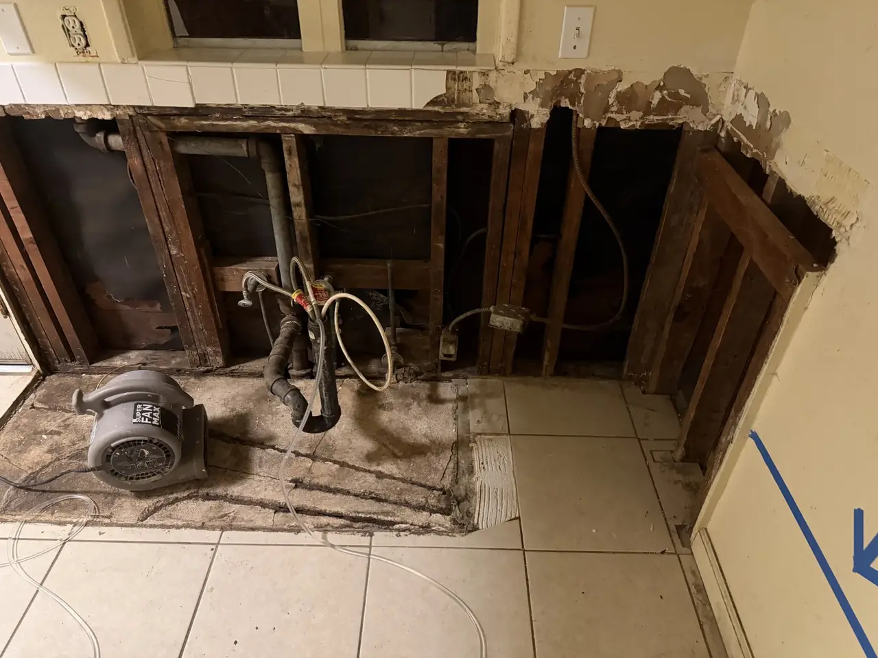 Open wall cavity showing framing, supply lines and drain piping, with an air mover running