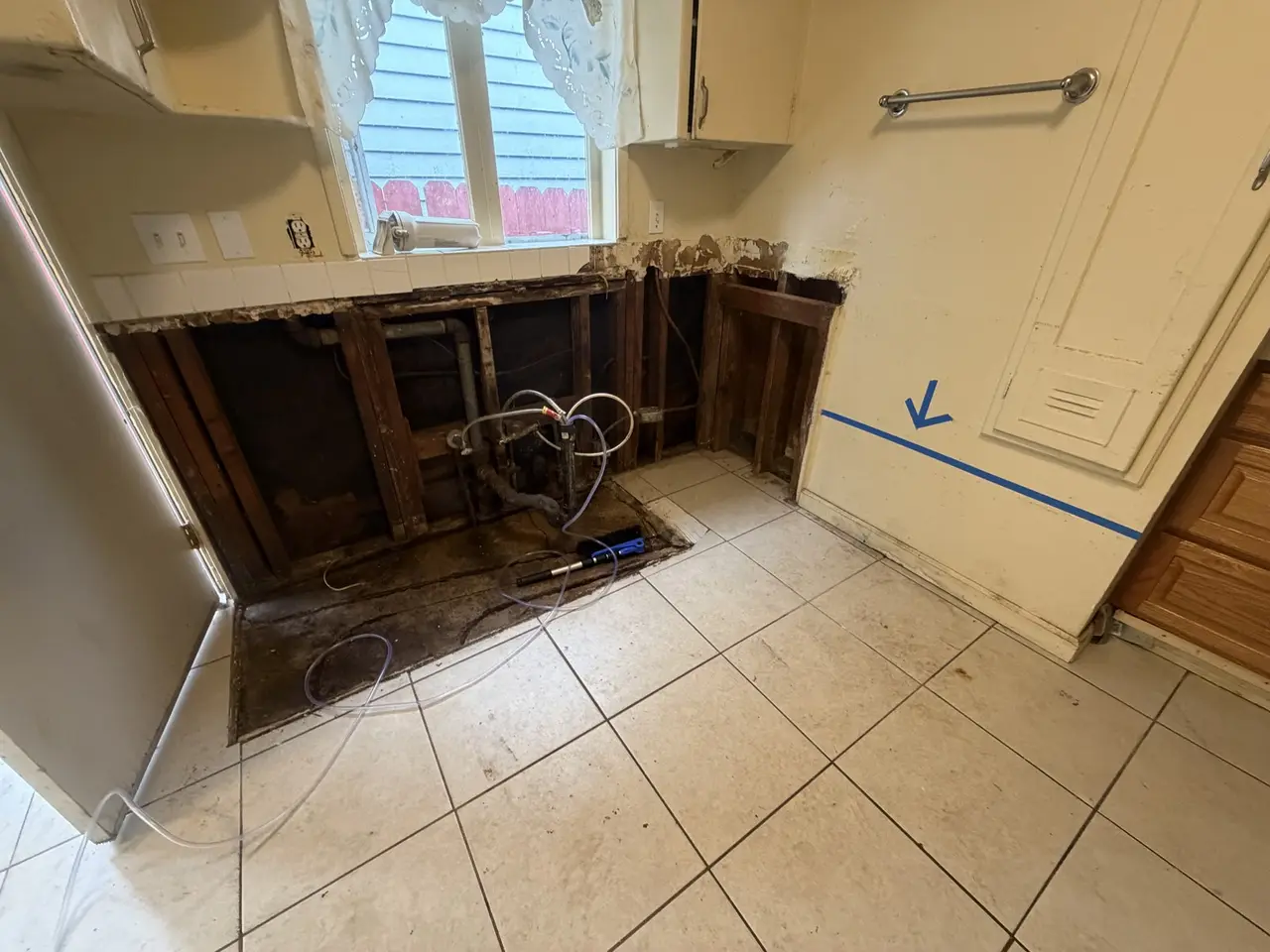 Lower cabinets removed and the wall opened to a straight line, exposing studs and plumbing